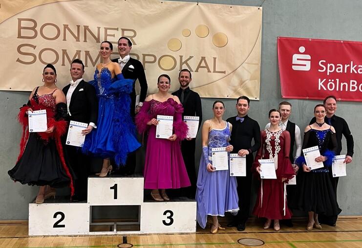 Sieger- und Teilnehmerpaar auf dem Treppchen beim Bonner Sommerpokal, mit Urkunden in der Hand und festlicher Kleidung.