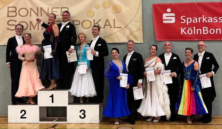 Siegerpaar und Teilnehmer des Bonner Sommerpokals stehen auf dem Treppchen mit Urkunden in festlicher Kleidung.