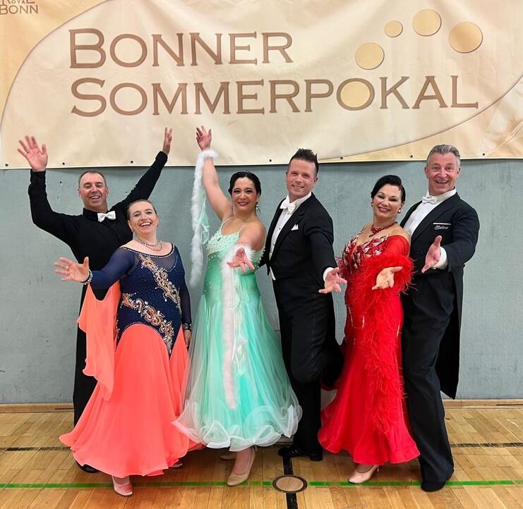 Sechs Tänzer in festlicher Kleidung posieren unter einem Banner für den Bonner Sommerpokal.