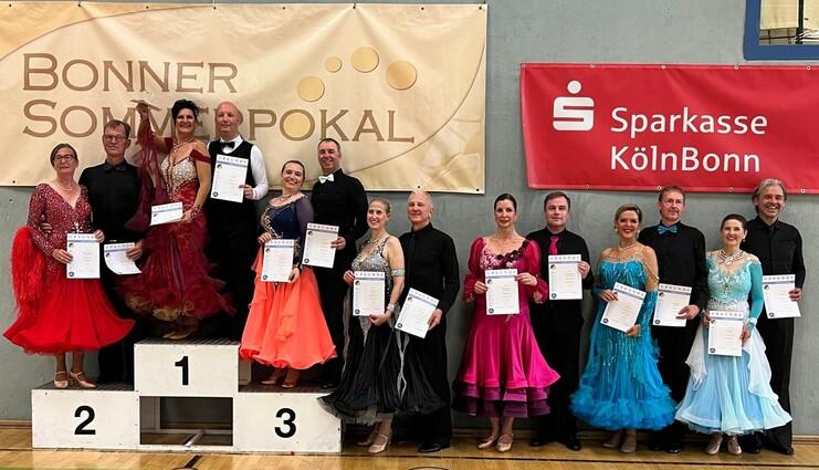 Gruppenfoto von Tänzern auf dem Siegertreppchen mit Urkunden, umgeben von festlichen Bannern.