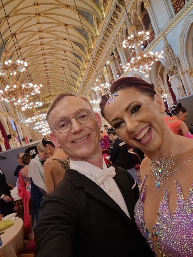 Selbstporträt von einem Mann im Smoking und einer Frau im glitzernden Kleid in einem festlichen Saal mit Kronleuchtern.