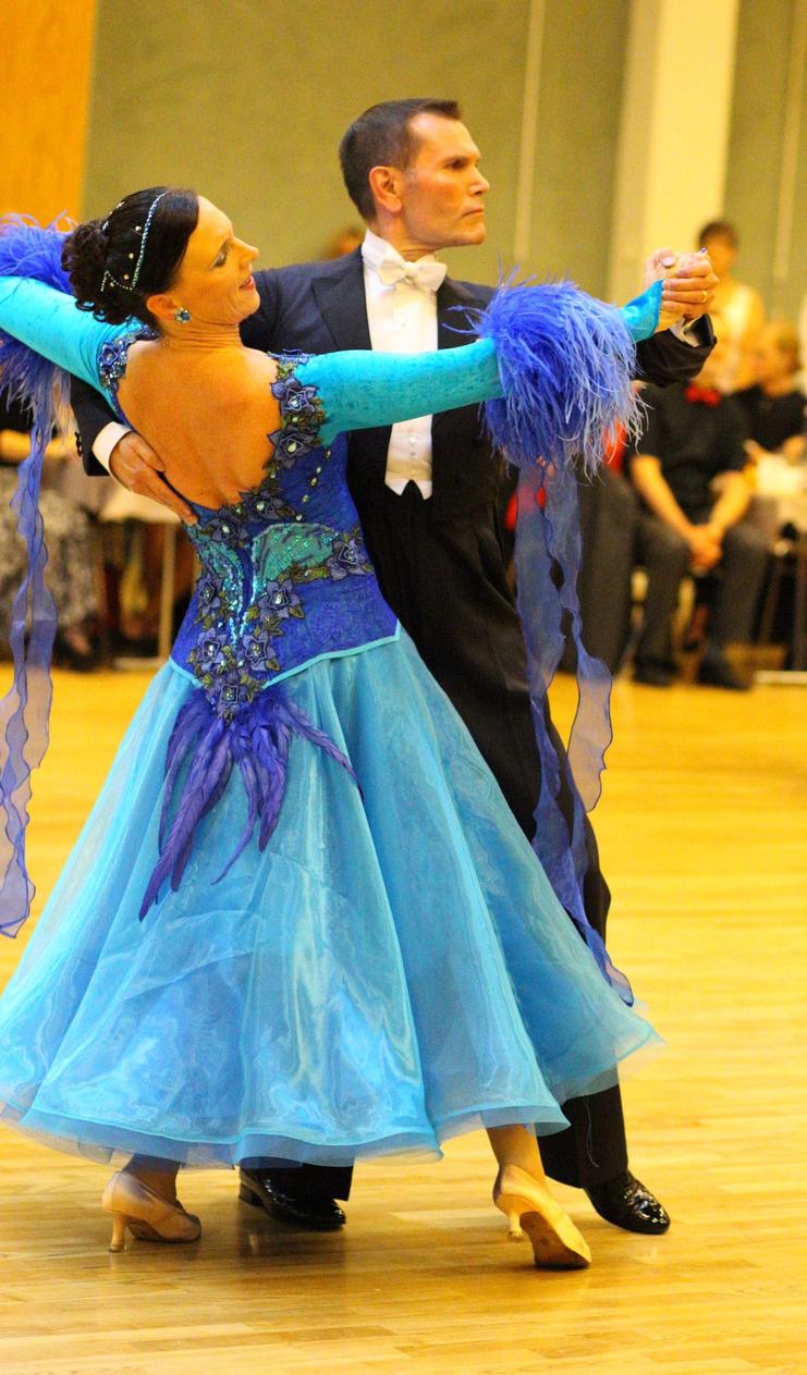 Tanzpaar in eleganter Kleidung vollführt einen langsamen Walzer auf einer Tanzfläche mit Holzfußboden.