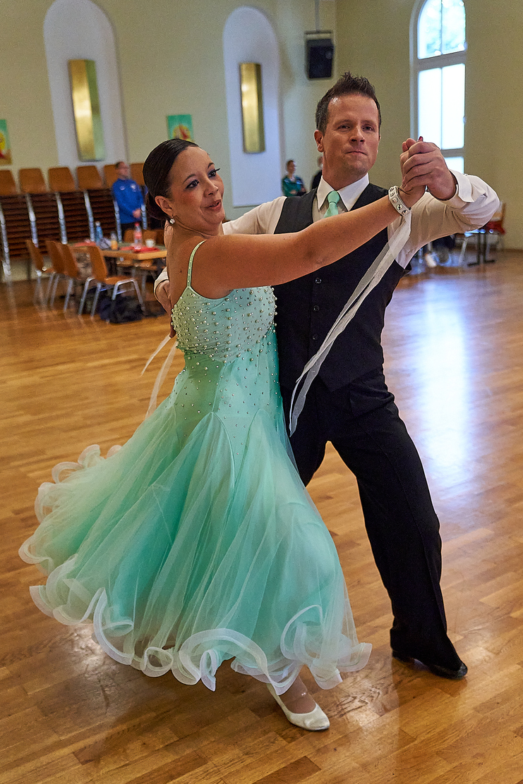 Tanzpaar in eleganter Kleidung, Tänzerin im mintgrünen Kleid, führt eine Walzerroutine auf einem Parkettboden aus.