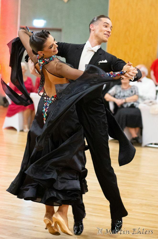 Tanzendes Paar in eleganter Kleidung, der Mann im schwarzen Anzug und die Frau in einem schwarzen Kleid mit farbigen Verzierungen.
