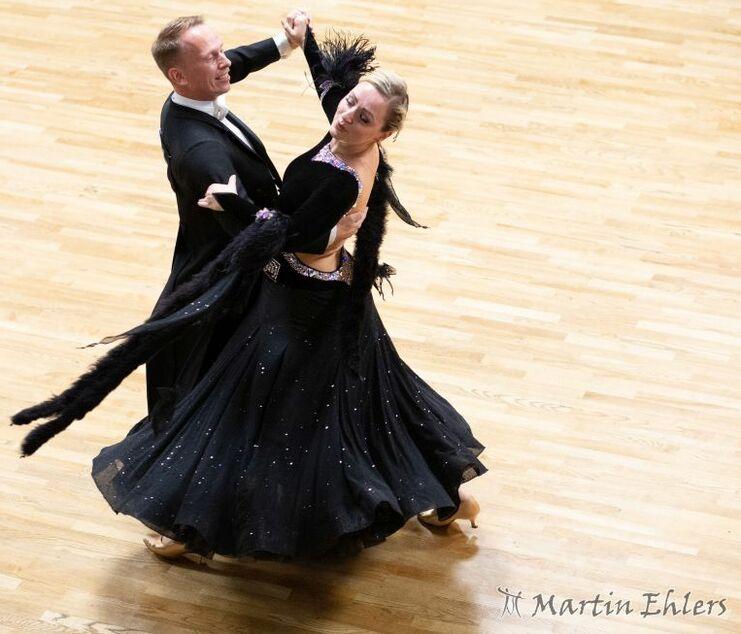 Tänzerpaar in eleganter Kleidung tanzt im Wettbewerb auf einem hölzernen Parkettboden.