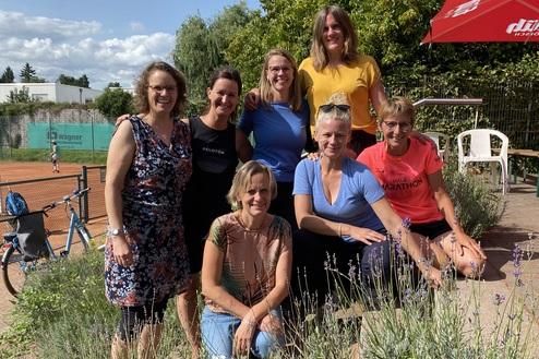 Gruppe von sieben Frauen in sportlicher Freizeitkleidung posiert im Freien neben blühenden Lavendelsträuchern.
