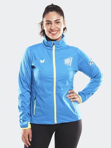 Lächelnde Frau in blauer Sportjacke mit gelben Akzenten, stehend vor einem hellen Hintergrund.