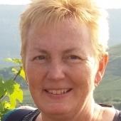 Nahaufnahme einer l&auml;chelnden Frau mit blonden Haaren, im Hintergrund eine gr&uuml;ne Landschaft.