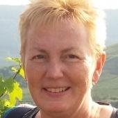 Nahaufnahme einer lächelnden Frau mit blonden Haaren, im Hintergrund eine grüne Landschaft.