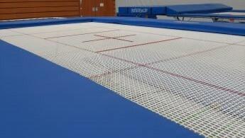 Nahaufnahme eines Trampolins mit blauer Umrandung und markierten Linien auf der Sprungfläche.