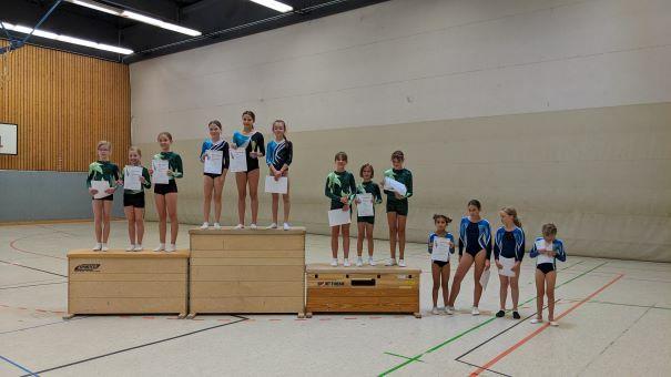 Gruppe von Turnerinnen mit Urkunden, die auf Podesten in einer Turnhalle stehen, von links in Sportanzügen.