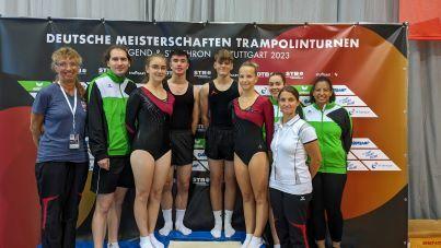Teamfoto von Trampolinturnern und Trainern vor einem Banner der Deutschen Meisterschaften in Stuttgart 2023.