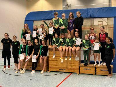 Gruppe von Turnerinnen in sportlicher Kleidung, posierend auf einer Matte mit Urkunden in den Händen.