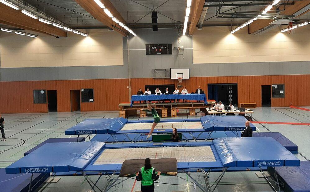 Trampolinspringerin springt von einem Trampolin mit Sportgericht im Hintergrund in einer Sporthalle.