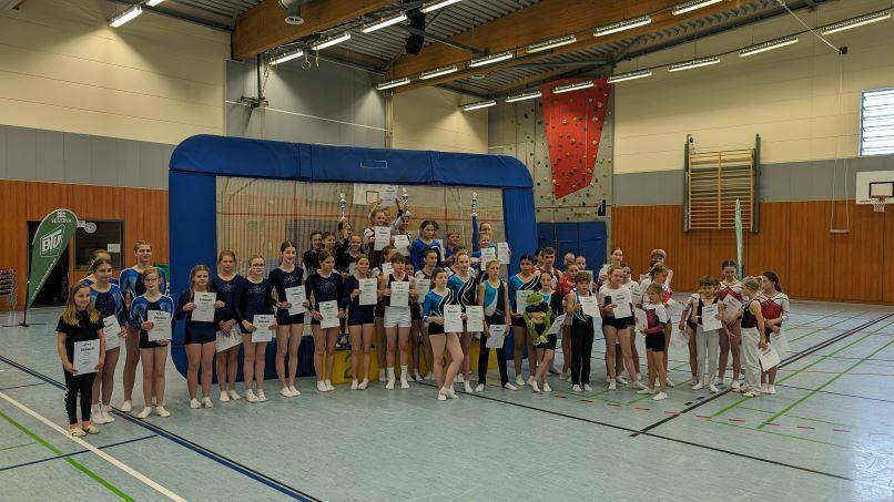 Gruppe von Turnerinnen hält Urkunden, stehen vor einem Sprunggerät in einer Sporthalle.