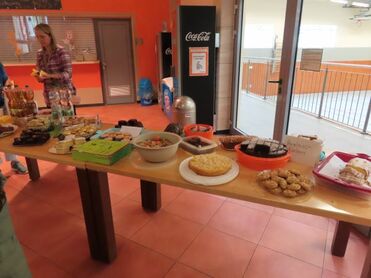 Buffet mit verschiedenen Speisen, darunter Kuchen, Plätzchen und Salat, auf einem Tisch in einem hellen Raum.