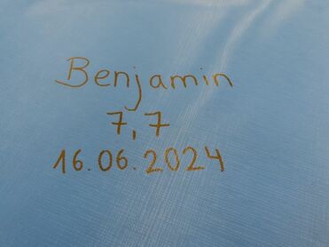Beschriftung auf blauer Fläche mit den Worten „Benjamin“, „7,7“ und „16.06.2024“ in goldener Schrift.