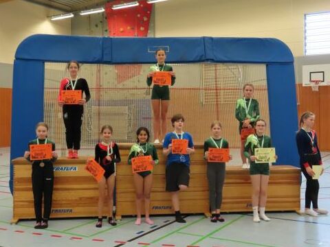 Gruppensieger im Turnerwettbewerb stehen mit Medaillen und Urkunden auf einer Siegerehrung im Sporthallen.