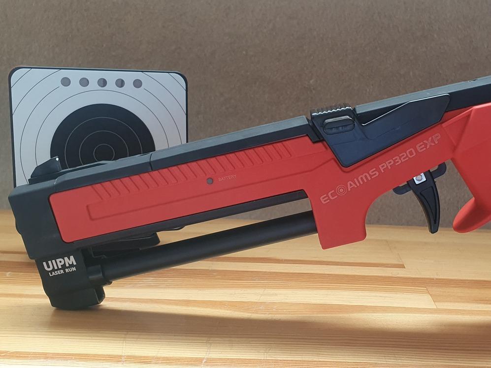 Nahaufnahme eines rot-schwarzen authentischen Laser-Trainingsgewehrs mit Zielscheibe im Hintergrund.