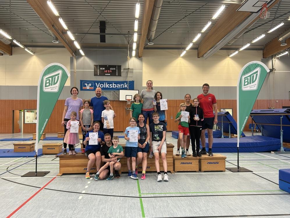 Gruppenfoto mit Kindern und Trainern in einer Sporthalle, alle halten Urkunden oder Medaillen, im Hintergrund Trampolins.