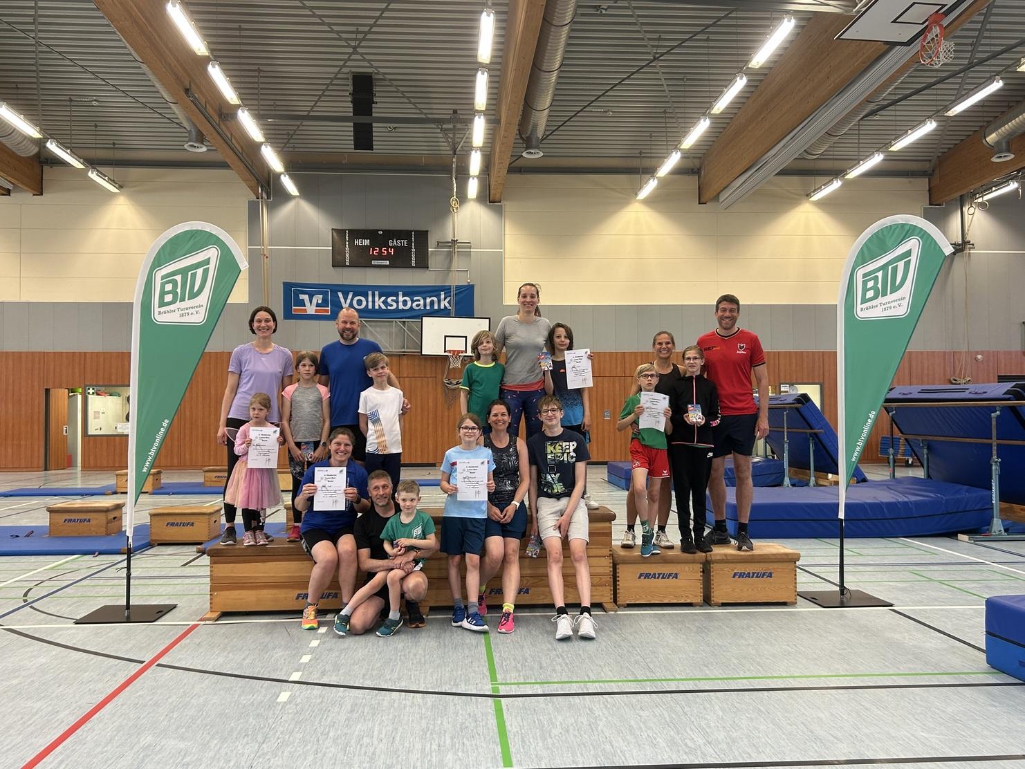 Gruppenfoto mit Kindern und Trainern in einer Sporthalle, alle halten Urkunden oder Medaillen, im Hintergrund Trampolins.