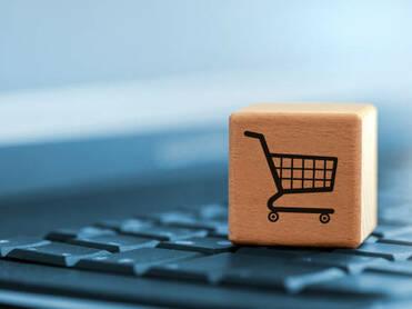 Holzblock mit Einkaufswagen-Symbol auf einer schwarzen Tastatur im Vordergrund.
