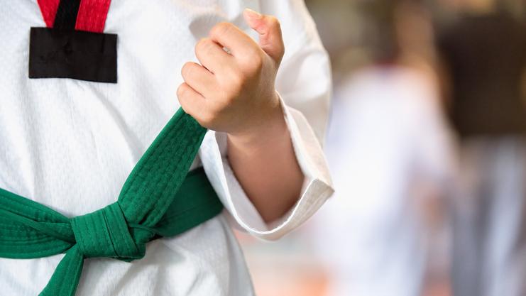 Nahaufnahme einer Hand, die einen grünen Gürtel an einem weißen Karateanzug hält.