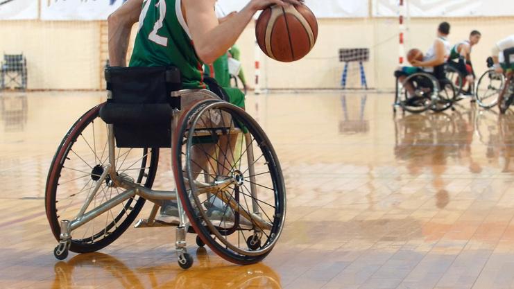Nahaufnahme eines Rollstuhlbasketballspielers, der den Ball in der Hand hält, im Sportumfeld mit anderen Spielern.