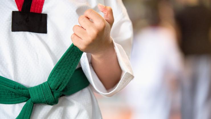 Nahaufnahme einer Hand, die einen grünen Gürtel an einem weißen Karateanzug hält.