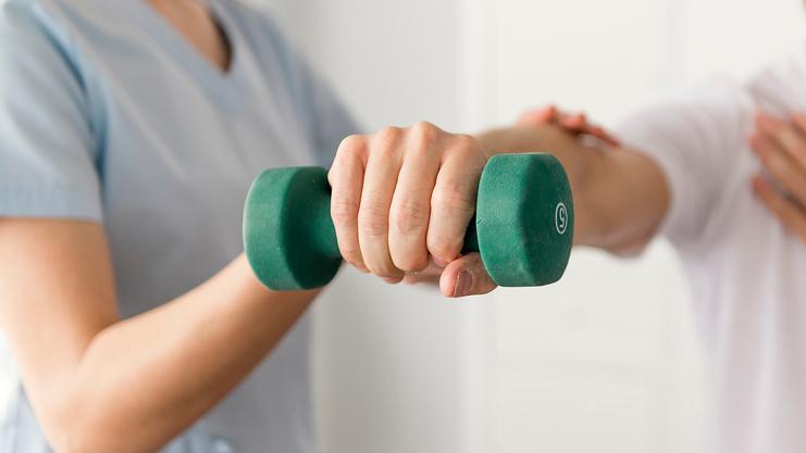 Physiotherapeutin hilft Mann beim Training mit einer grünen Hantel in einer modernen Behandlungseinrichtung.