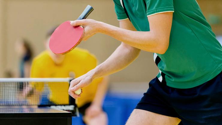 Nahaufnahme eines Tischtennisspielers in grünem Trikot, der bereit ist, einen Ball auf einem Tisch zu schlagen.