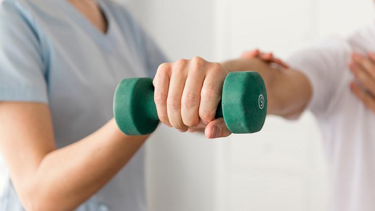 Physiotherapeutin hilft Mann beim Training mit einer grünen Hantel in einer modernen Behandlungseinrichtung.