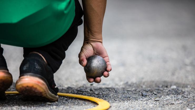 Nahaufnahme einer Hand, die eine Kugel hält, mit einem gelben Kreis auf dem Boden im Hintergrund.