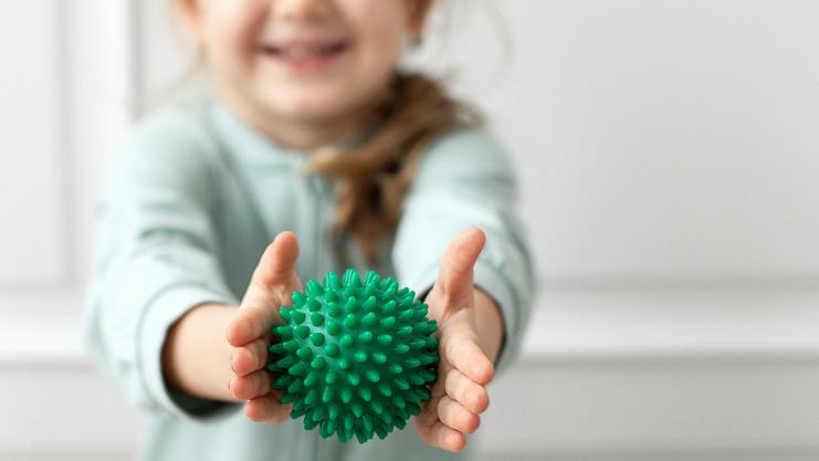 Lachenendes Kind hält einen grünen, stacheligen Stressball mit beiden Händen vor sich.