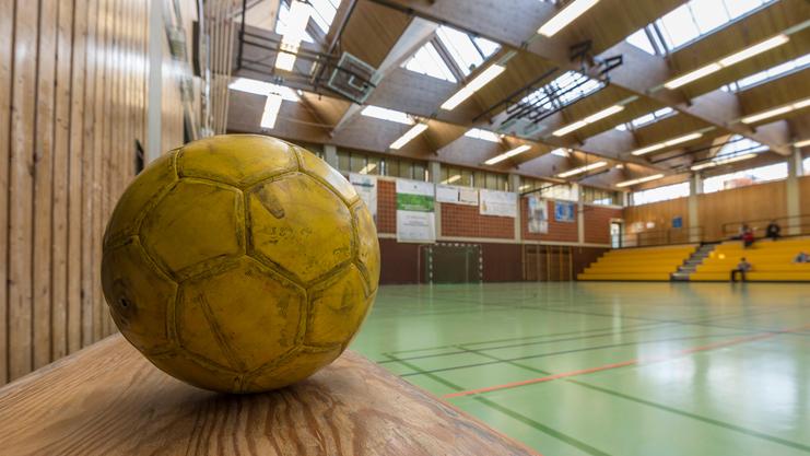 Nahaufnahme eines gelben Fußballes auf einer Holzfläche in einer Sporthalle mit grünem Boden.