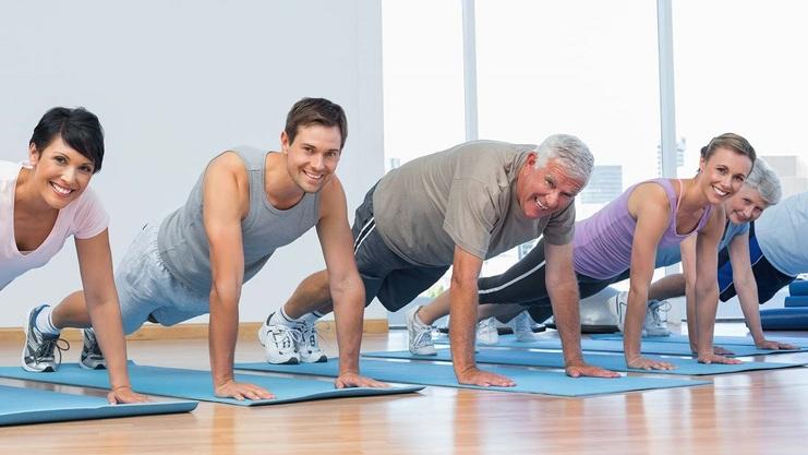 Sechs Personen machen Liegestütze auf blauen Matten in einem modernen Fitnessraum mit großen Fenstern.