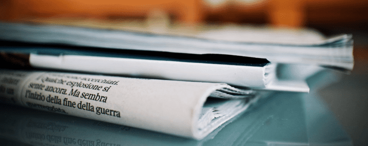 Nahaufnahme mehrerer übereinander liegender Zeitungen auf einem Glastisch mit unscharfem Hintergrund.