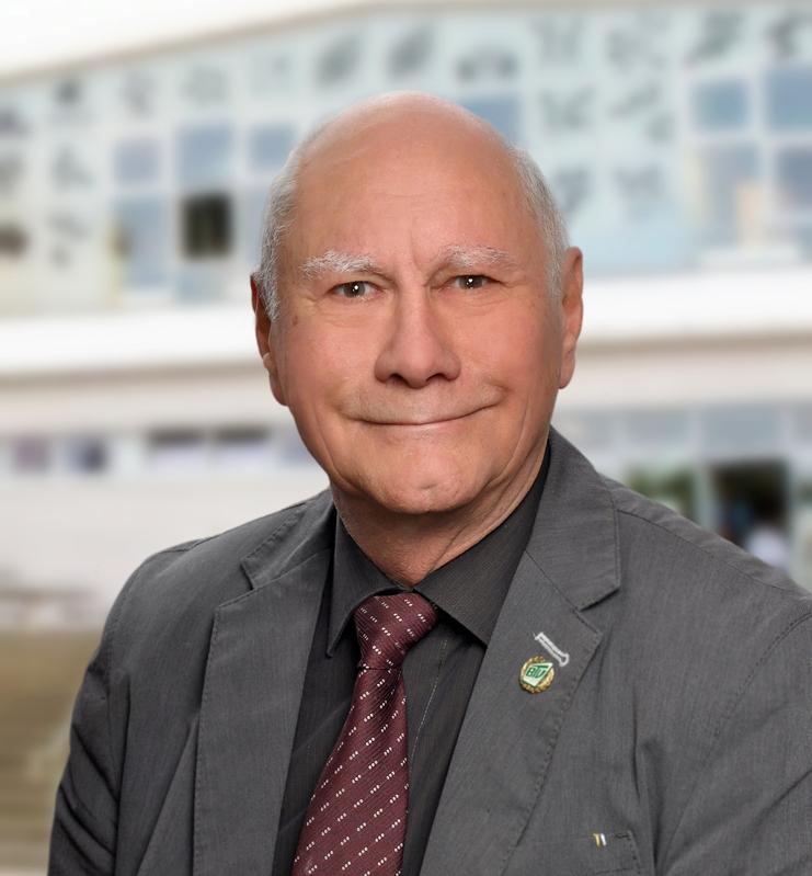 Porträt eines älteren Mannes mit Graufaser-Haar, Anzugjacke und Krawatte vor einem unscharfen Hintergrund.