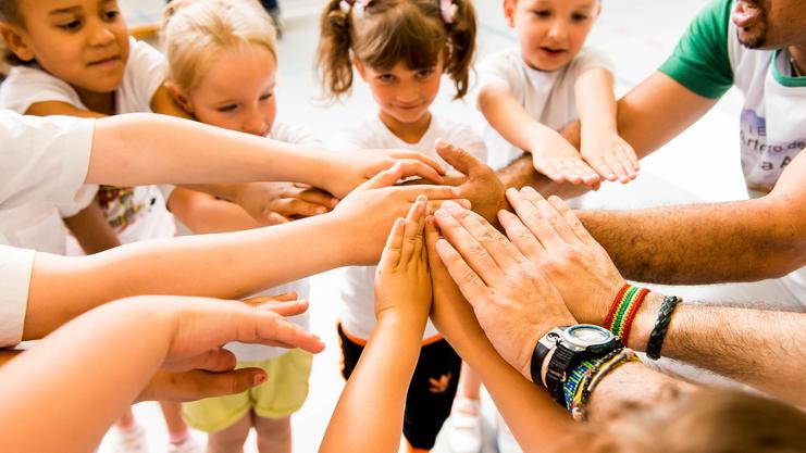Kinder und Erwachsene legen ihre Hände in einem Kreis zusammen, symbolisieren Zusammenarbeit und Gemeinschaft.